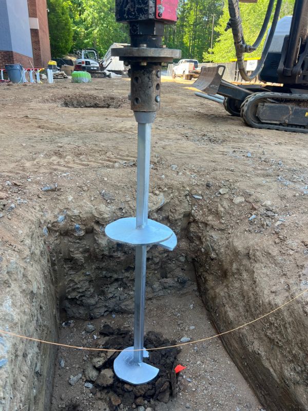 Double-helix pile being driven into an excavated footing trench