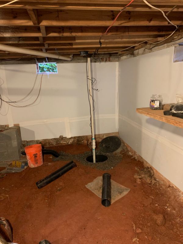 Sump basin with discharge pipe and drain piping being installed in a basement with a soil floor